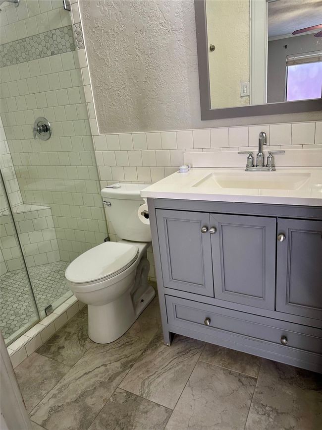 Full bathroom featuring a textured wall, vanity, a stall shower, a wainscoted wall, and tile walls | Image 26