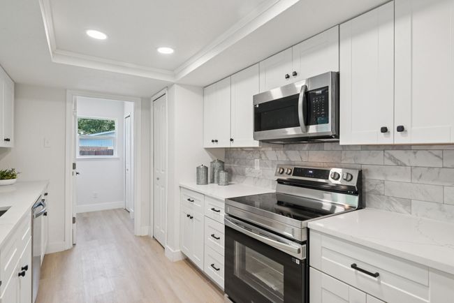 Kitchen with stainless steel appliances, light wood-style flooring, backsplash, white cabinets, and light stone countertops | Image 23