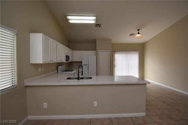 Kitchen featuring a peninsula, lofted ceiling, visible vents, and white appliances | Image 6