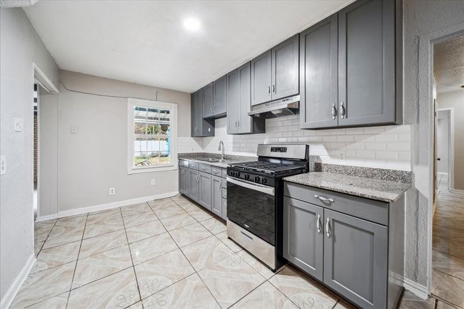 Kitchen featuring stainless steel gas stove, gray cabinets, under cabinet range hood, and decorative backsplash | Image 11