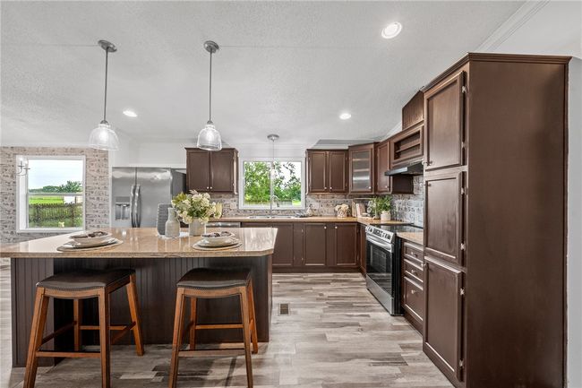 Kitchen with stainless steel appliances, under cabinet range hood, a textured ceiling, backsplash, and a kitchen bar | Image 6
