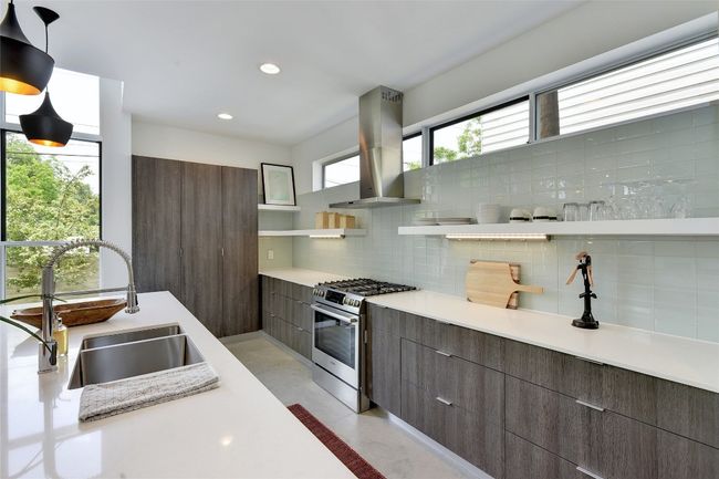 Kitchen featuring open shelves, island exhaust hood, a sink, stainless steel gas range oven, and decorative backsplash | Image 8