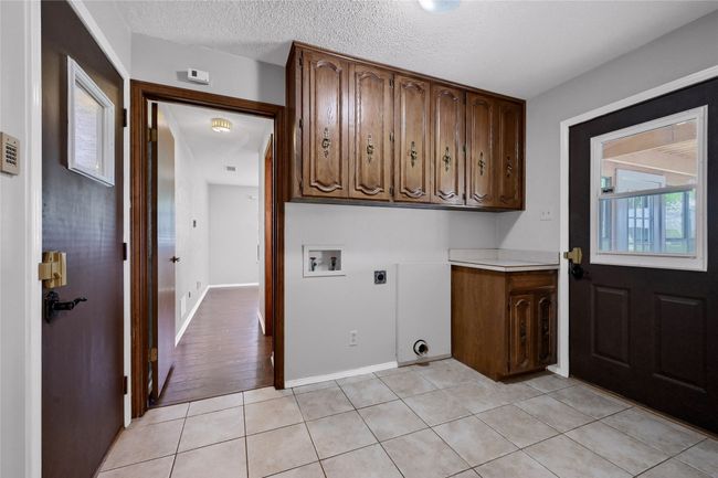 Washroom featuring hookup for an electric dryer, light tile patterned floors, a textured ceiling, hookup for a washing machine, and cabinet space | Image 17
