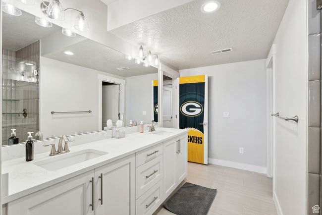 Full bath featuring baseboards, a textured ceiling, double vanity, and a sink | Image 25