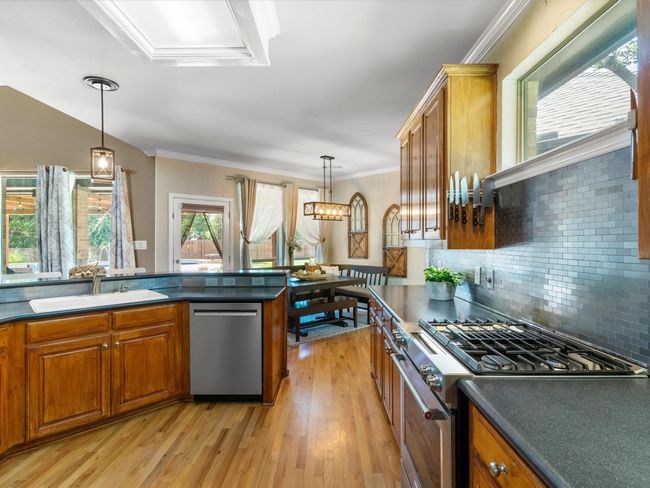 Kitchen featuring stainless steel appliances, brown cabinetry, dark countertops, light wood-style floors, and crown molding | Image 9