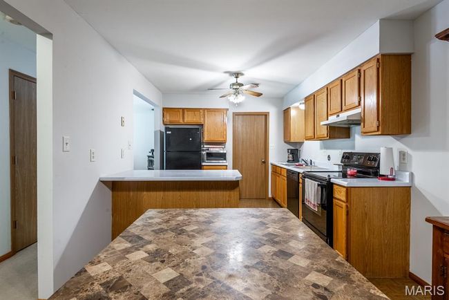 Kitchen with black appliances, under cabinet range hood, a peninsula, ceiling fan, and brown cabinets | Image 7