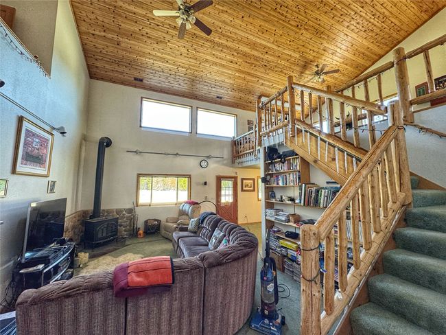 Carpeted living room featuring high vaulted ceiling, a wood stove, wood ceiling, and a ceiling fan | Image 22