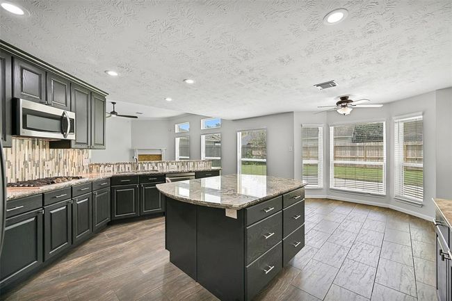 Walls of windows bathe the kitchen and breakfast room in natural light, while the open layout to the family room and wraparound breakfast bar makes entertaining a breeze. | Image 13