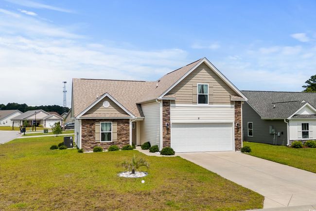 Traditional-style home featuring stone siding, central air condition unit, concrete driveway, an attached garage, and a front lawn | Image 26