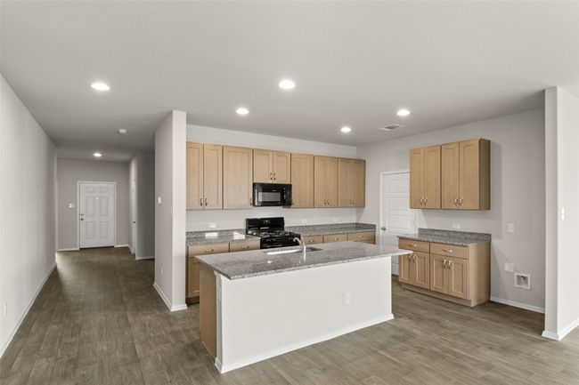 Kitchen with visible vents, a sink, dark wood-style flooring, an island with sink, and black appliances | Image 4
