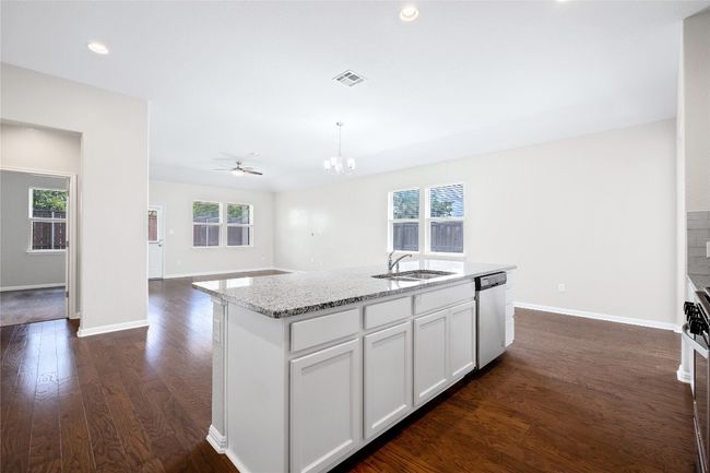 Kitchen with stainless steel dishwasher, a chandelier, dark wood-style floors, white cabinets, and light stone counters | Image 14