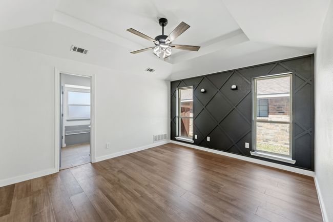 Empty room with a tray ceiling, visible vents, ceiling fan, and wood finished floors | Image 26