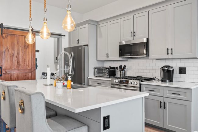 Kitchen featuring a barn door, appliances with stainless steel finishes, gray cabinetry, and tasteful backsplash | Image 8