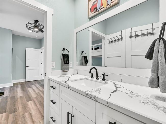 This stylish Jack & Jill bath features a quartz-top vanity with black hardware and a beautifully tiled tub/shower combo with built-in niches and frameless glass—perfectly positioned between the two custom bunk rooms for added convenience and comfort. | Image 23