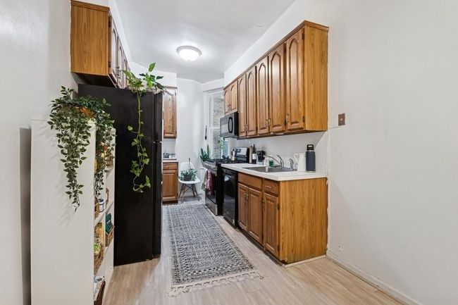 Kitchen with a sink, light countertops, light wood-type flooring, brown cabinetry, and black appliances | Image 7