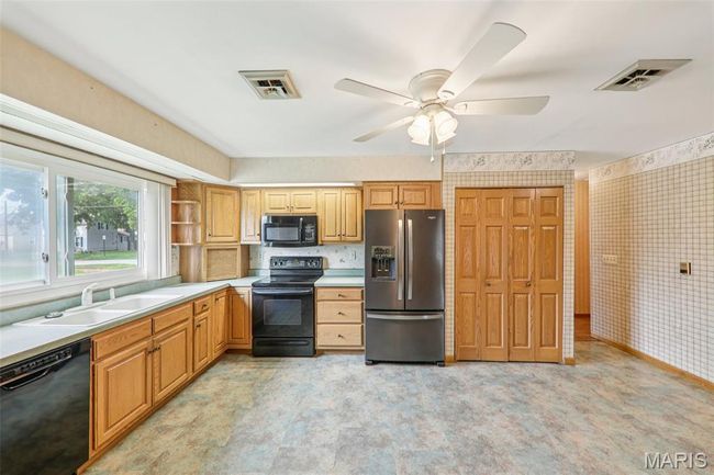 Kitchen with black appliances, wallpapered walls, a ceiling fan, light countertops, and open shelves | Image 15
