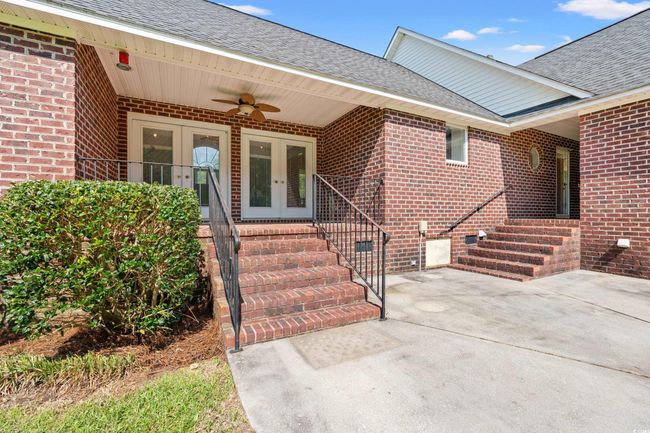 View of exterior entry featuring french doors, ceiling fan, brick siding, roof with shingles, and a patio | Image 21