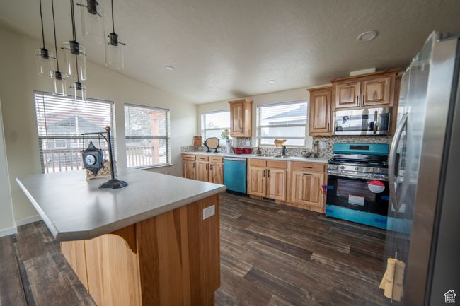 Kitchen featuring lofted ceiling, dark wood-style floors, light countertops, a center island, and appliances with stainless steel finishes | Image 7