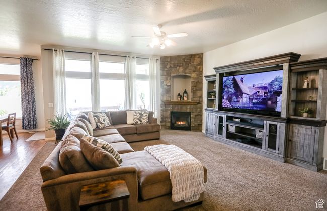 Living area with ceiling fan, a stone fireplace, and a textured ceiling | Image 16