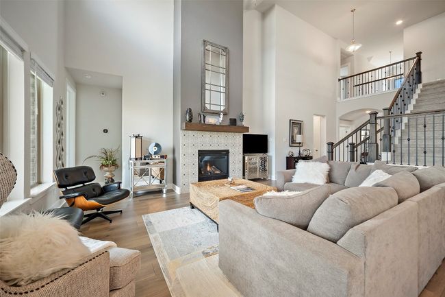 Living room featuring a towering ceiling, a glass covered fireplace, wood finished floors, stairs, and recessed lighting | Image 17