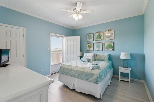 This serene secondary guest bedroom features calming blue walls and coastal-inspired decor, creating a tranquil retreat. The room offers direct access to a private deck, perfect for enjoying morning coffee or evening sunsets. Ample natural light enhances the airy atmosphere, while the thoughtful layout provides both comfort and style. Ideal for guests or family, this space combines relaxation with beautiful outdoor access. | Image 10