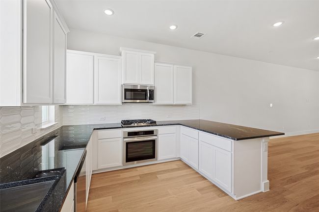 Kitchen featuring light hardwood / wood-style floors, white cabinetry, stainless steel appliances, and dark stone countertops | Image 5
