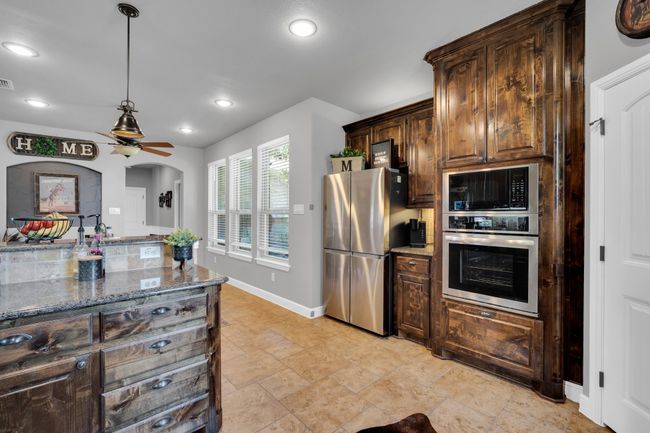 Kitchen with appliances with stainless steel finishes, dark brown cabinets, stone counters, and light tile patterned flooring | Image 9