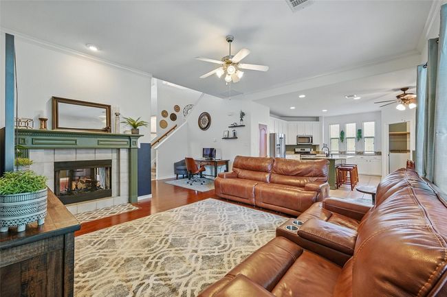 Living area with a ceiling fan, light wood-type flooring, stairs, a fireplace, and crown molding | Image 8