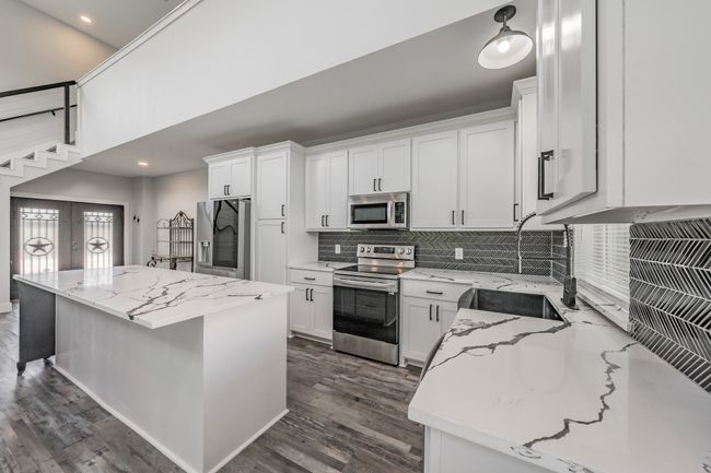 Kitchen with appliances with stainless steel finishes, tasteful backsplash, a sink, light stone countertops, and dark wood-style floors | Image 23