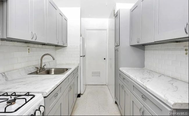 Kitchen featuring decorative backsplash, light floors, freestanding refrigerator, gray cabinets, and light stone counters | Image 5