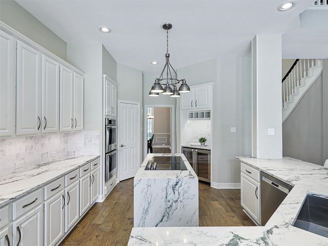 Kitchen with stainless steel appliances, white cabinets, light stone countertops, a chandelier, and recessed lighting | Image 16
