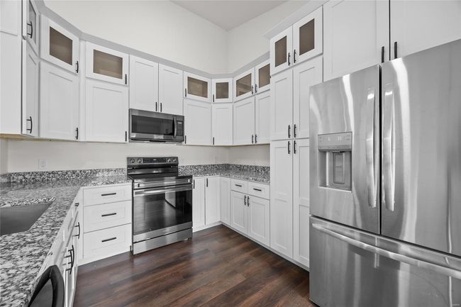 Kitchen with glass insert cabinets, dark wood-type flooring, white cabinets, light stone counters, and stainless steel appliances | Image 28