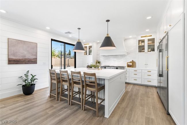 Kitchen with light wood-type flooring, a kitchen island, white cabinetry, and custom range hood | Image 11