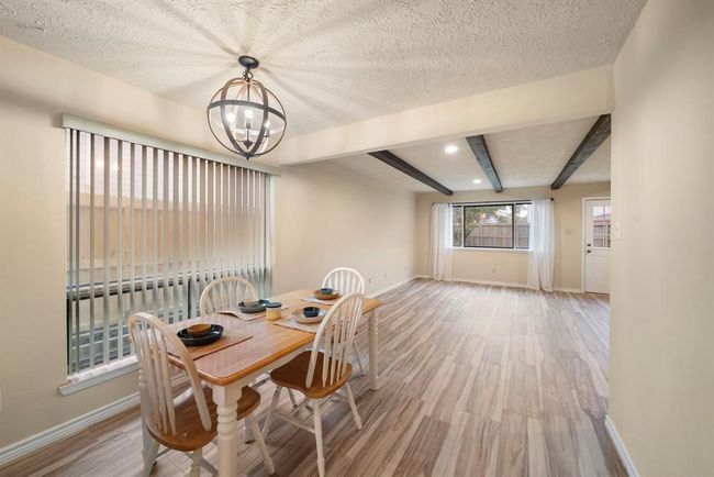 Large windows and vertical blinds flood the spacious dining area with natural light, while wood-style tile flooring and exposed ceiling beams flow seamlessly into the adjacent living space. | Image 14