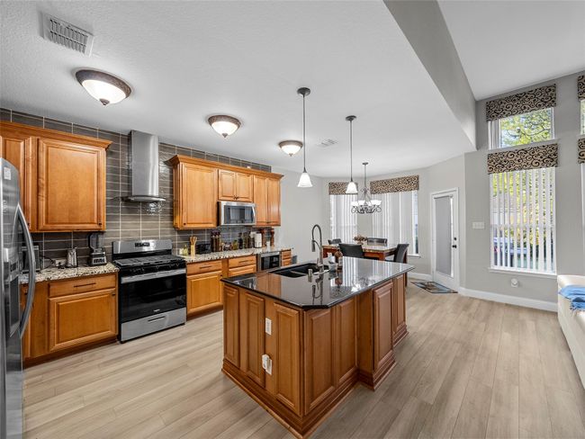 Kitchen with stainless steel appliances, visible vents, a sink, light wood-style floors, and wall chimney exhaust hood | Image 17