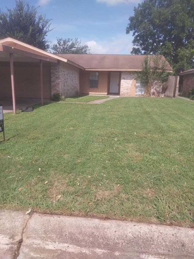 This photo shows a single-story brick house with a gabled roof. The front yard features a grassy lawn and walkway leading to the entrance. There are a few mature trees and fenced back yard. The house has a simple, inviting exterior. | Image 45
