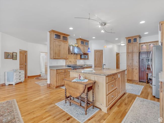 Kitchen with range hood, an island with sink, a sink, light wood-style floors, and appliances with stainless steel finishes | Image 13