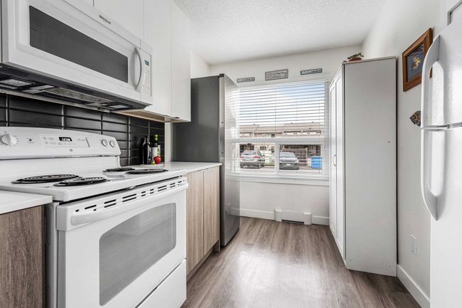 Kitchen with white appliances, light wood-style flooring, modern cabinets, and a textured ceiling | Image 9