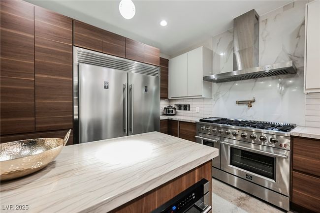 Kitchen with high end appliances, modern cabinets, wall chimney range hood, and backsplash | Image 14