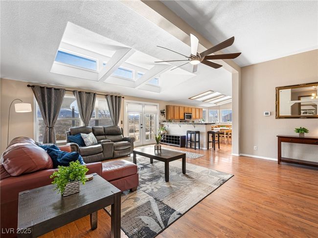 Living area with baseboards, vaulted ceiling with skylight, light wood-style floors, a textured ceiling, and a ceiling fan | Image 13