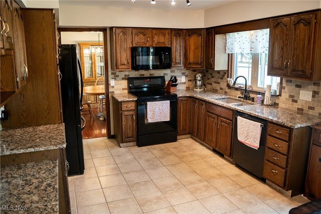 Kitchen featuring black appliances, decorative backsplash, light tile patterned flooring, and light granite counters | Image 19