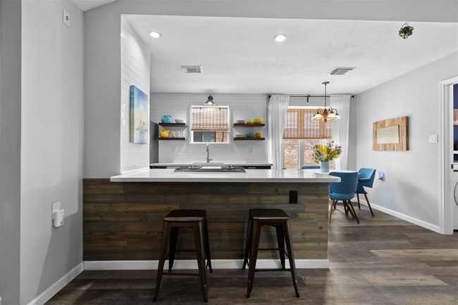 A modern, open-concept kitchen and dining area. The kitchen features sleek white countertops, a built-in cooktop, and stylish open shelving. | Image 15