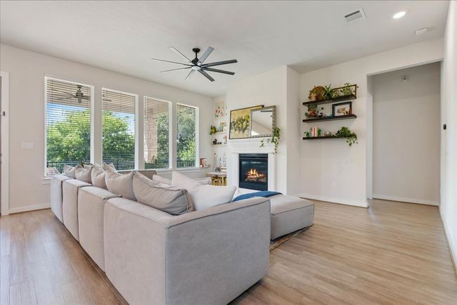 Living area with a glass covered fireplace, baseboards, light wood-style flooring, visible vents, and ceiling fan | Image 13