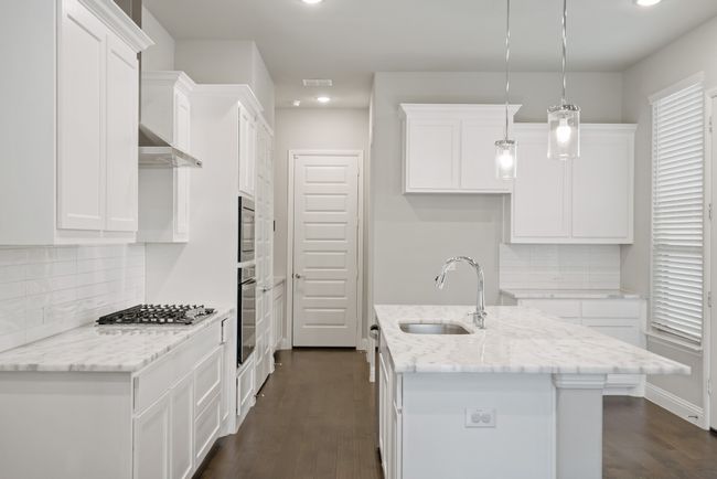 Kitchen featuring dark wood-style flooring, stainless steel appliances, backsplash, a sink, and white cabinets | Image 11