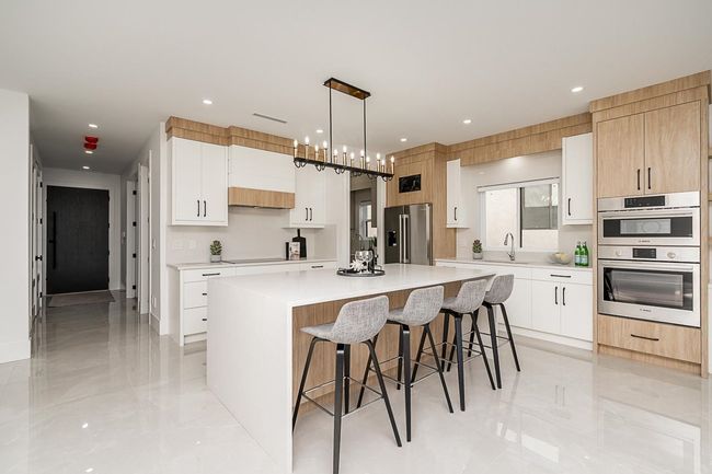 Kitchen featuring stainless steel appliances, a center island, modern cabinets, a kitchen breakfast bar, and light countertops | Image 5