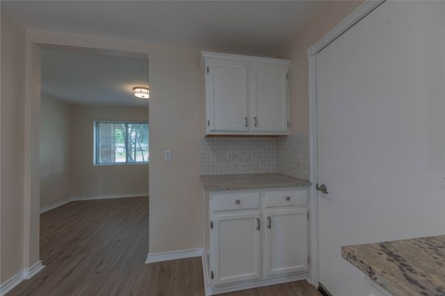 Kitchen featuring white cabinets, decorative backsplash, wood finished floors, baseboards, and light stone countertops | Image 6