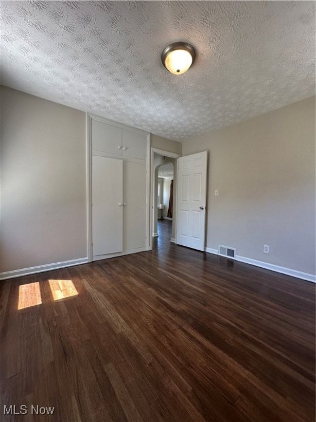 Unfurnished room featuring arched walkways, baseboards, visible vents, a textured ceiling, and dark wood-type flooring | Image 22