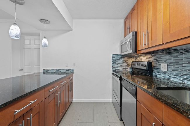 Kitchen with brown cabinetry, baseboards, dark stone counters, stainless steel appliances, and backsplash | Image 12