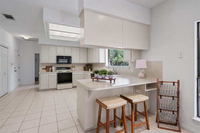 Kitchen with range with electric cooktop, light countertops, visible vents, black microwave, and a peninsula | Image 12