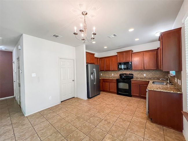 Kitchen featuring black appliances, tasteful backsplash, a chandelier, light stone counters, and light tile patterned floors | Image 5
